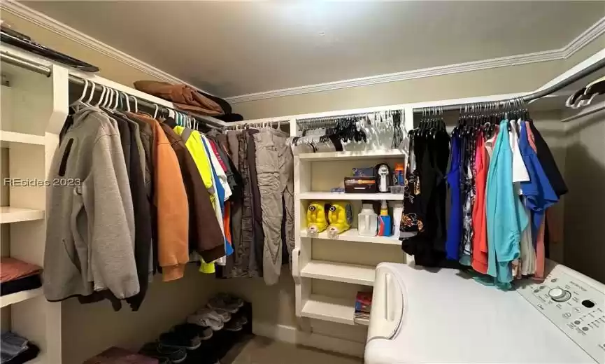 Overall, this primary closet with custom wood shelving and an adjacent laundry area offers a perfect blend of elegance and functionality. It's a space where you can not only keep your wardrobe impeccably organized but also maintain the freshness of your clothing with ease.