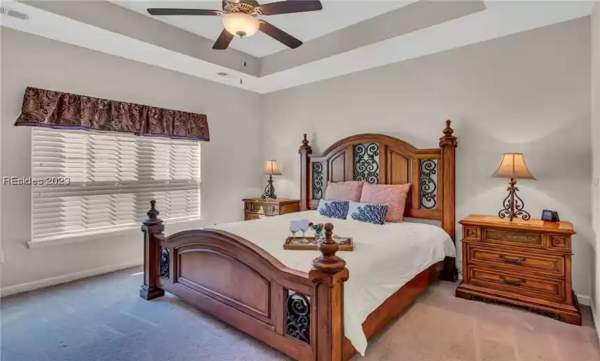 Large master bedroom has attractive neutral carpeting, attractive ceiling, and ceiling fan/light.