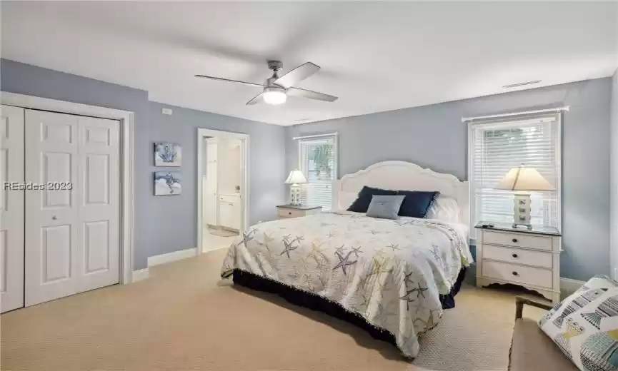 Bedroom with ensuite bathroom, a closet, ceiling fan, and light colored carpet