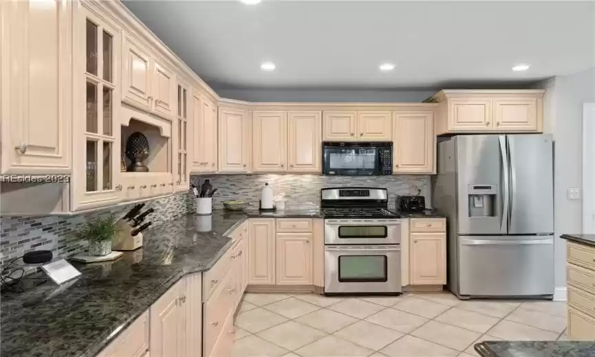 Kitchen with dark stone countertops, light tile flooring, tasteful backsplash, and stainless steel appliances