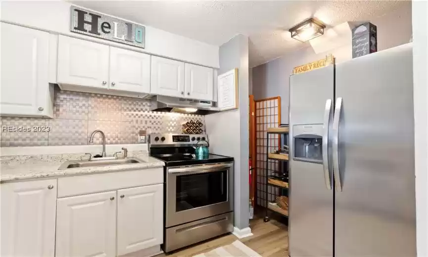Kitchen with sink, tasteful backsplash, stainless steel appliances, light wood-type flooring, and white cabinetry