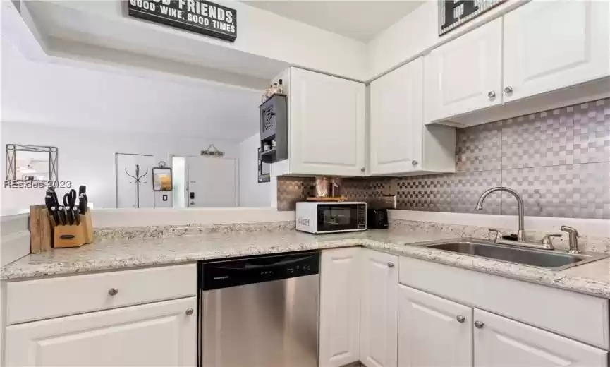 Kitchen featuring dishwasher, sink, light stone countertops, tasteful backsplash, and white cabinetry