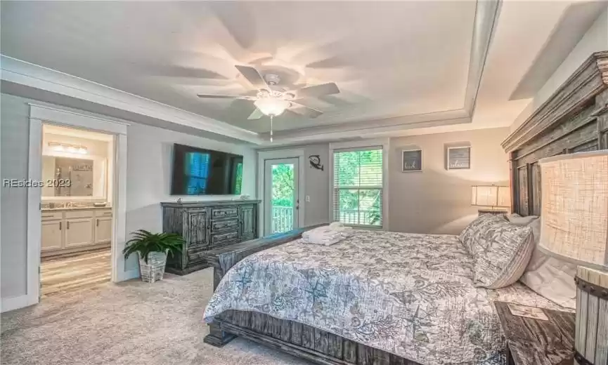 Bedroom featuring a raised ceiling, ensuite bath, ceiling fan, and light colored carpet