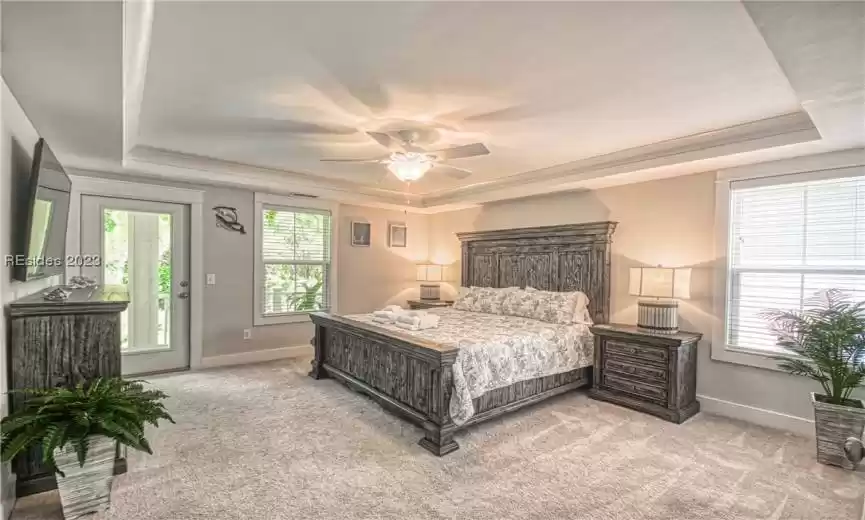 Carpeted bedroom with a tray ceiling, ceiling fan, and access to outside