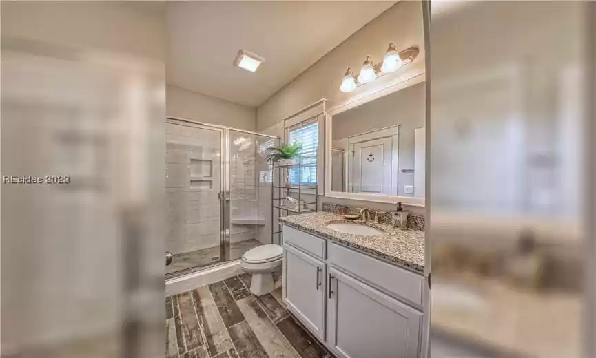 Bathroom with wood-type flooring, oversized vanity, toilet, and a shower with shower door