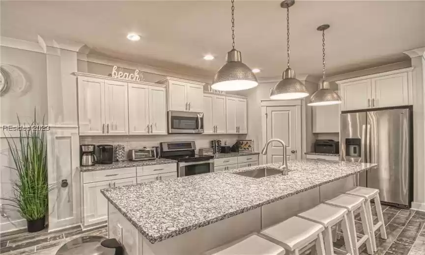 Kitchen featuring hanging light fixtures, sink, appliances with stainless steel finishes, tasteful backsplash, and a center island with sink