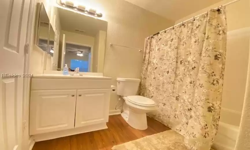 Full bathroom featuring vanity, toilet, wood-type flooring, shower / bath combination with curtain, and ceiling fan