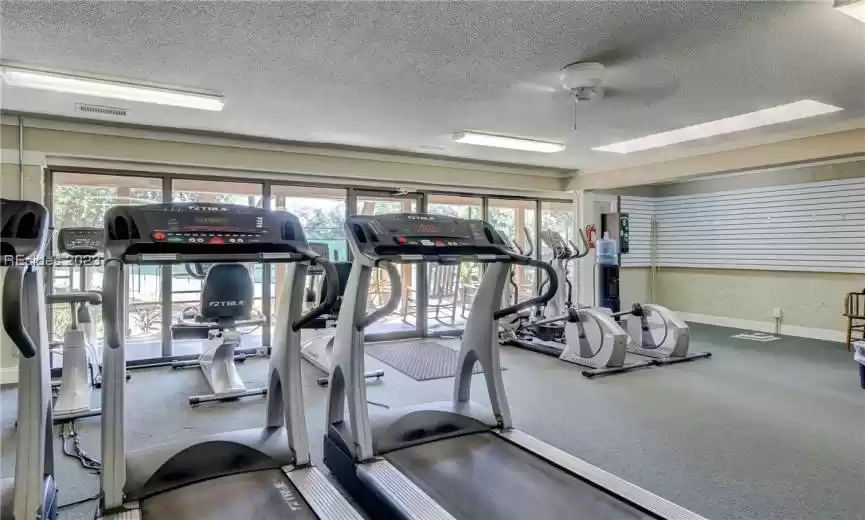 Gym featuring ceiling fan, a textured ceiling, and carpet flooring