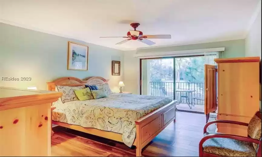 King bedroom suite with light hardwood style flooring, access to private balcony exterior and ceiling fan