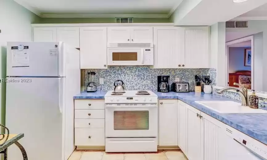 Kitchen featuring light tile floors, white cabinets, sink, and white appliances
