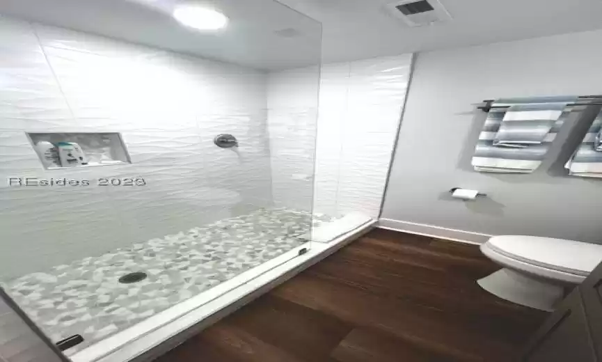 Bathroom with toilet, tiled shower, and LVP wood-type flooring