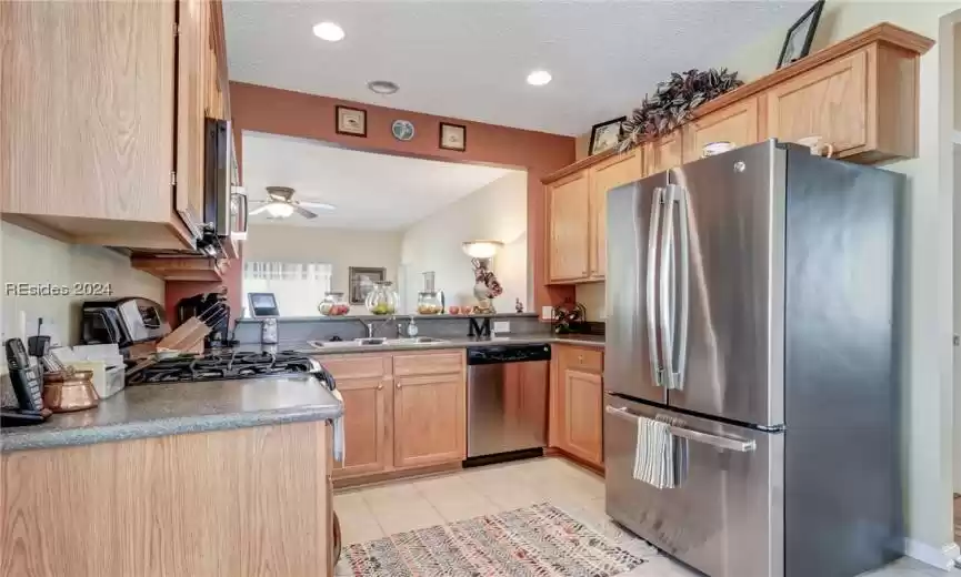 Kitchen featuring a textured ceiling, ceiling fan, sink, light tile floors, and stainless steel appliances