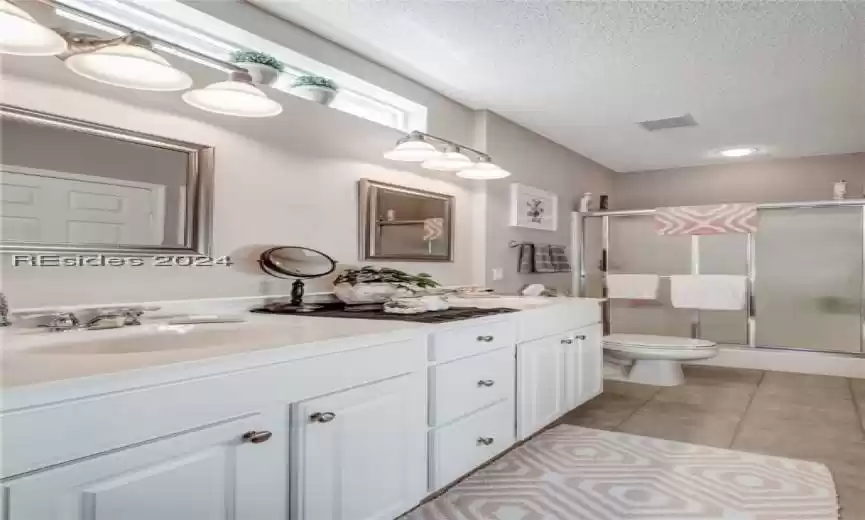 Bathroom featuring a textured ceiling, double sink vanity, toilet, a shower with shower door, and tile flooring
