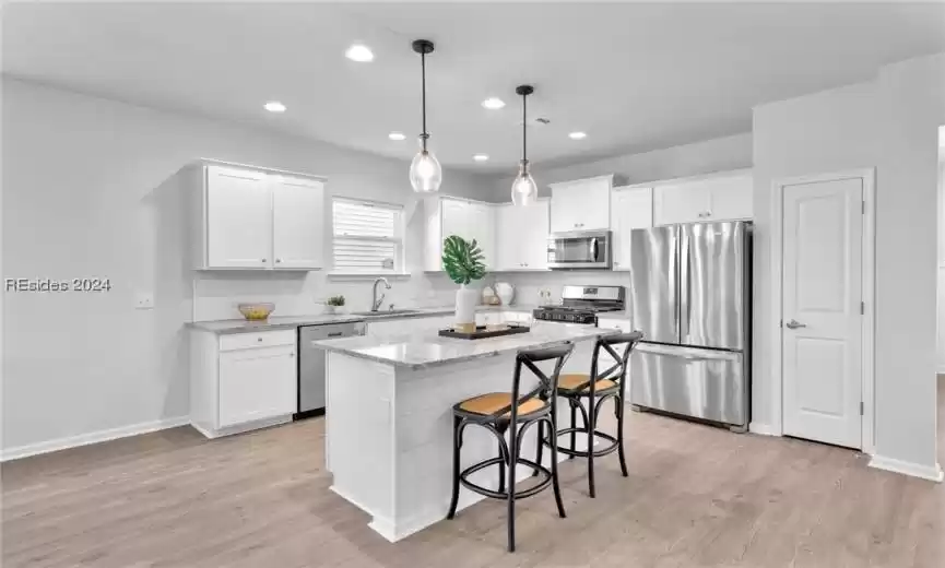 Kitchen featuring light hardwood / wood-style floors, white cabinetry, sink, stainless steel appliances, and decorative light fixtures