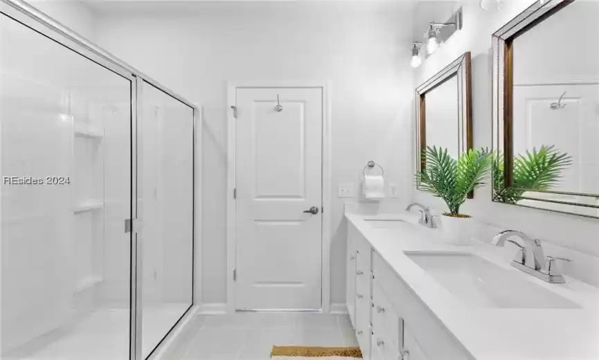 Bathroom featuring a shower with door, large vanity, tile flooring, and double sink