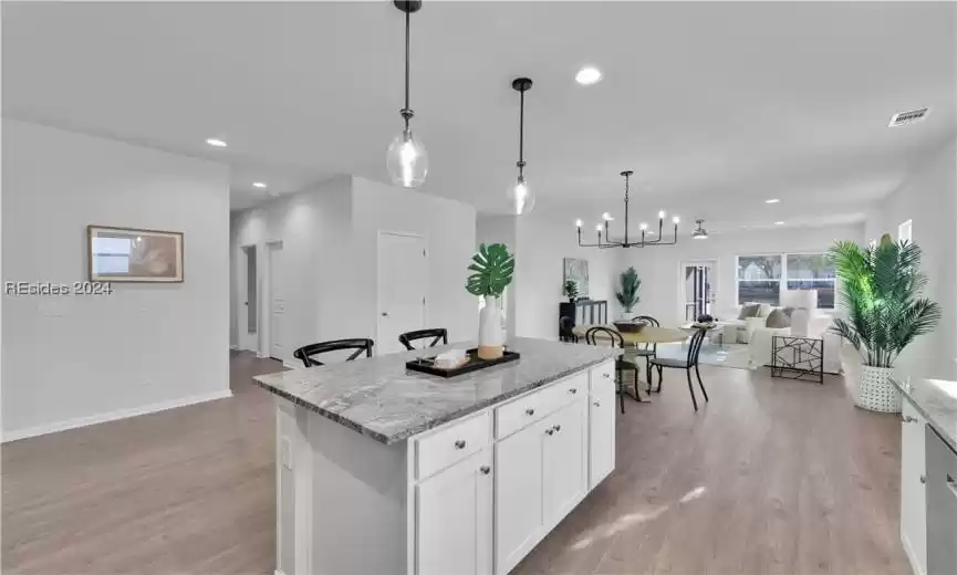 Kitchen featuring pendant lighting, an inviting chandelier, light stone counters, white cabinets, and light hardwood / wood-style LVP floors