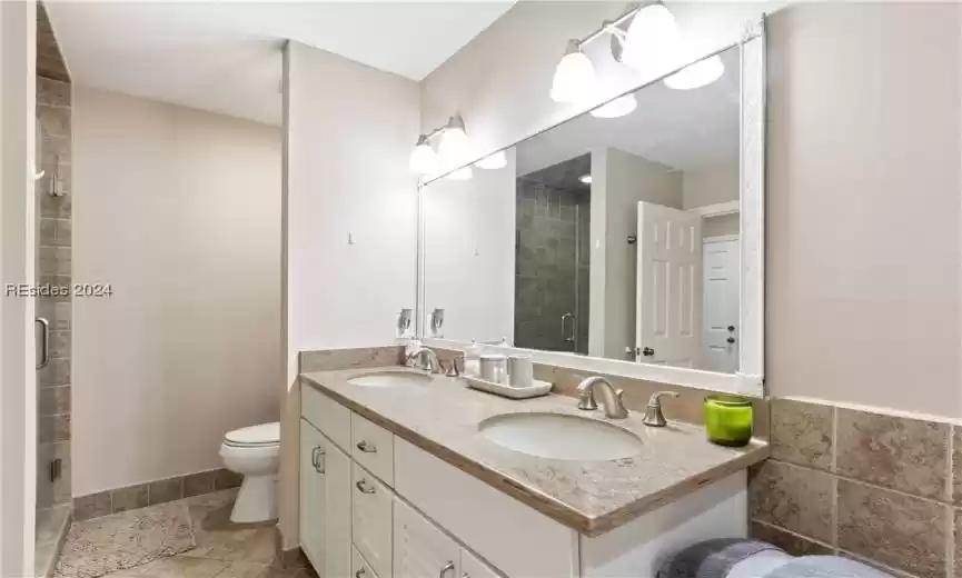 Bathroom featuring toilet, double sink vanity, a shower with shower door, and tile flooring