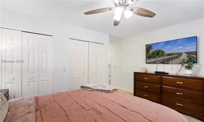Unfurnished bedroom with light carpet, ceiling fan, and two closets
