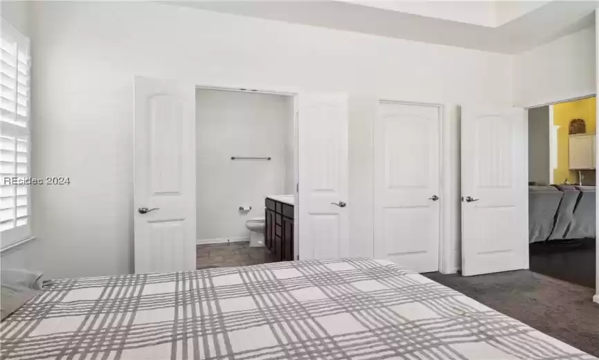 Unfurnished bedroom featuring ensuite bathroom, dark colored carpet, multiple windows, and a closet