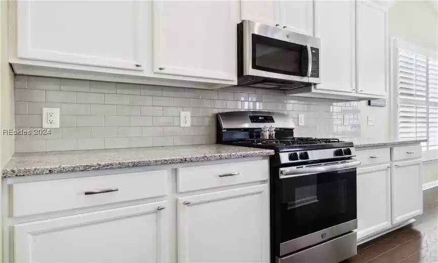 Kitchen with appliances with stainless steel finishes, dark wood-type flooring, light stone counters, and white cabinets