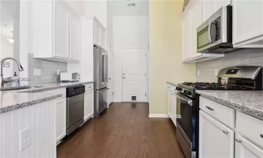 Kitchen featuring dark hardwood / wood-style flooring, stainless steel appliances, white cabinetry, tasteful backsplash, and sink