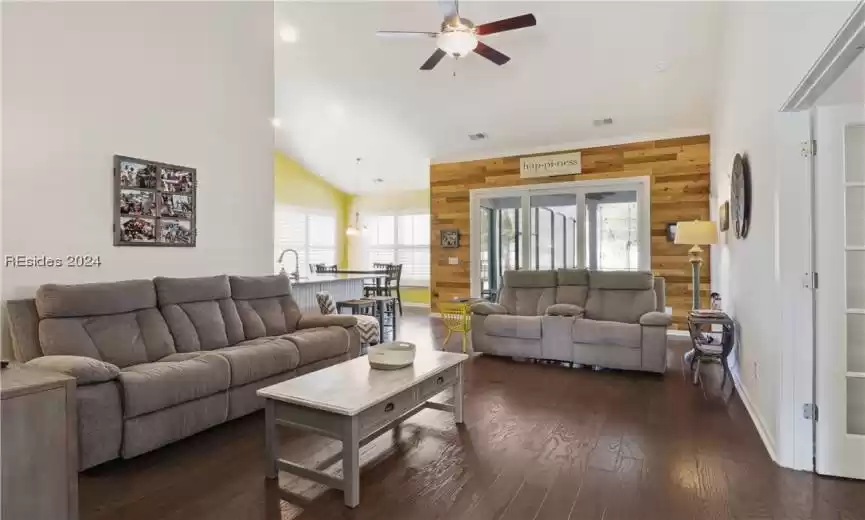 Living room featuring dark hardwood / wood-style flooring, high vaulted ceiling, ceiling fan, and wood walls