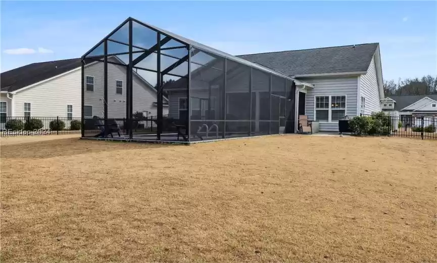 Rear view of house featuring a lawn, glass enclosure, and a patio area