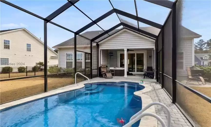 View of pool with glass enclosure, ceiling fan, and a patio