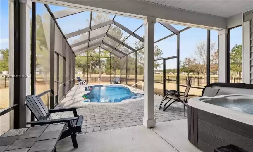 View of pool featuring glass enclosure, a hot tub, and a patio