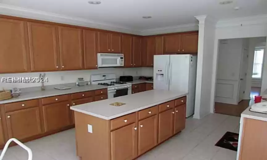 Kitchen featuring white appliances, light tile floors, a kitchen island, and crown molding