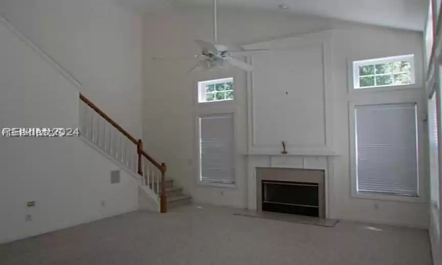 Unfurnished living room with high vaulted ceiling, ceiling fan, and light colored carpet