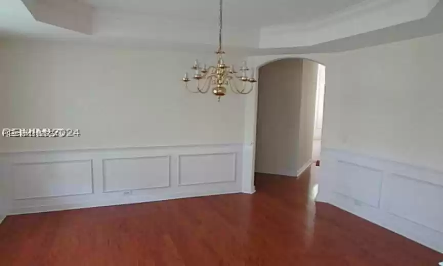 Spare room featuring a chandelier, ornamental molding, a tray ceiling, and dark hardwood / wood-style flooring