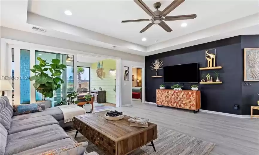 Living room with light wood-type flooring, a tray ceiling, and ceiling fan
