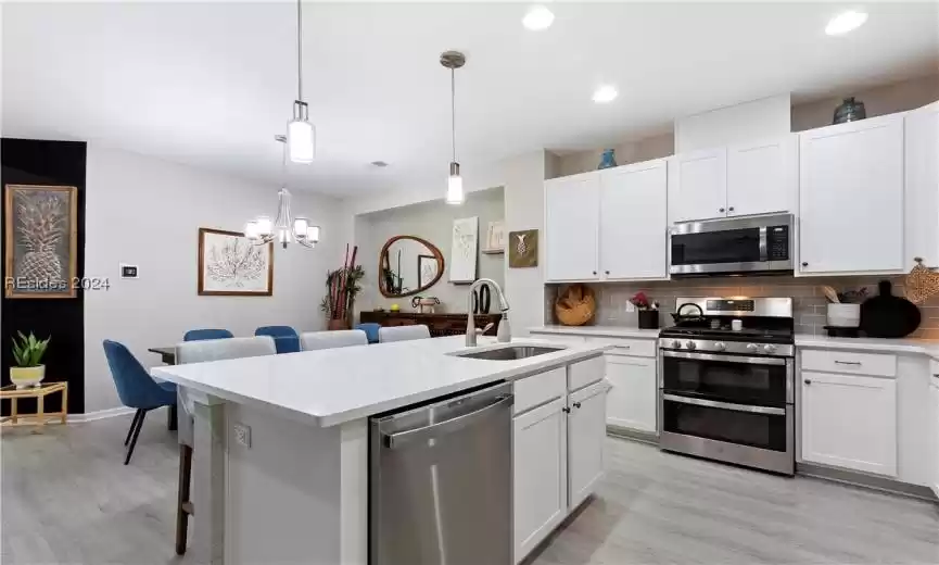 Kitchen featuring hanging light fixtures, appliances with stainless steel finishes, white cabinets, and sink