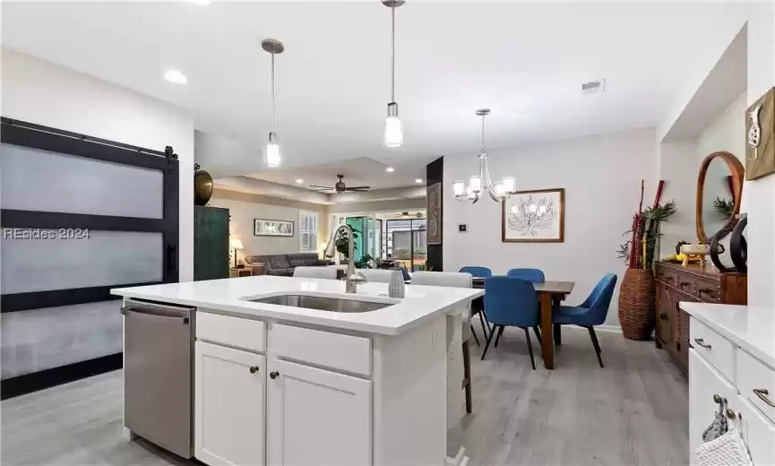 Kitchen featuring ceiling fan with notable chandelier, white cabinets, stainless steel dishwasher, light hardwood / wood-style flooring, and decorative light fixtures