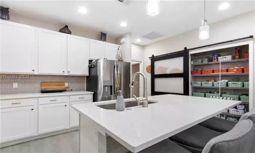 Kitchen featuring stainless steel refrigerator with ice dispenser, tasteful backsplash, a barn door, light hardwood / wood-style floors, and decorative light fixtures