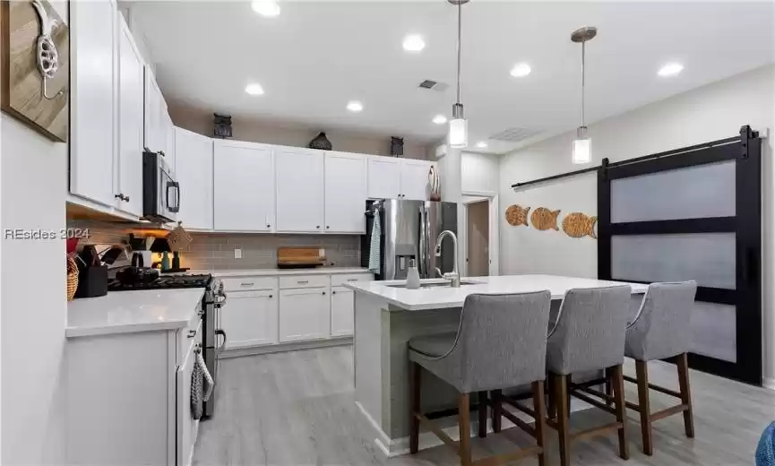 Kitchen featuring hanging light fixtures, tasteful backsplash, a barn door, white cabinetry, and stainless steel appliances