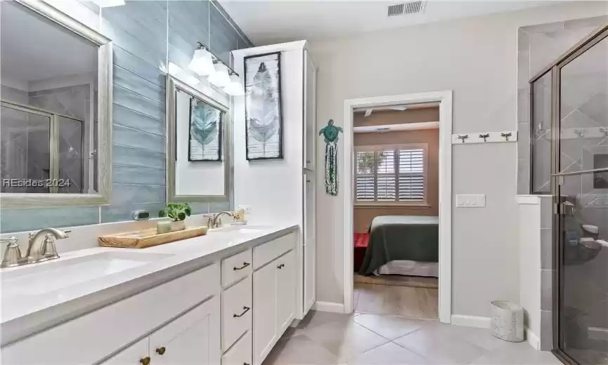 Bathroom with a shower with shower door, tile flooring, double sink, and vanity with extensive cabinet space