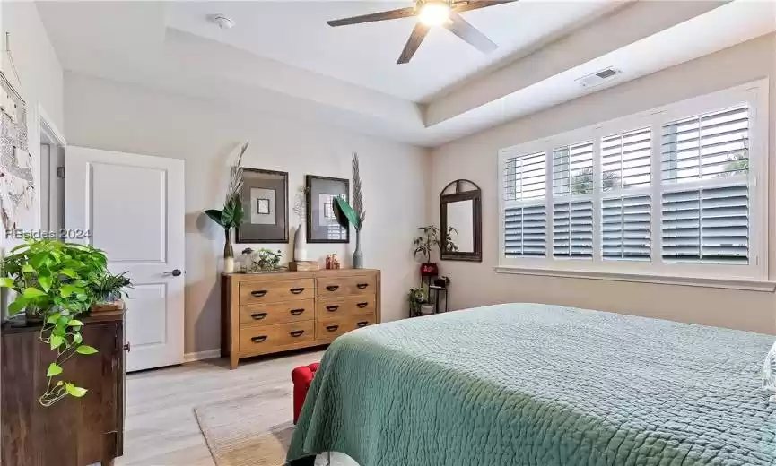 Bedroom with light hardwood / wood-style floors, ceiling fan, and a raised ceiling