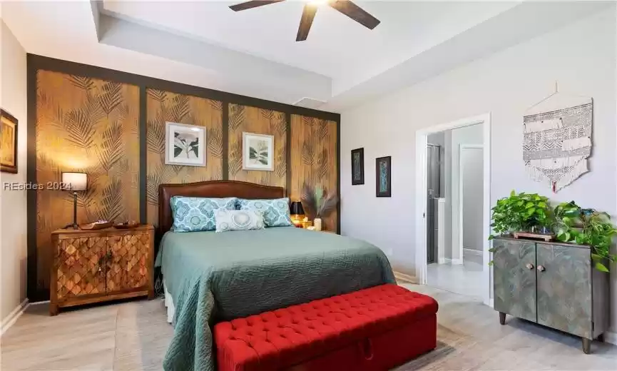 Bedroom featuring light wood-type flooring, ceiling fan, and a raised ceiling
