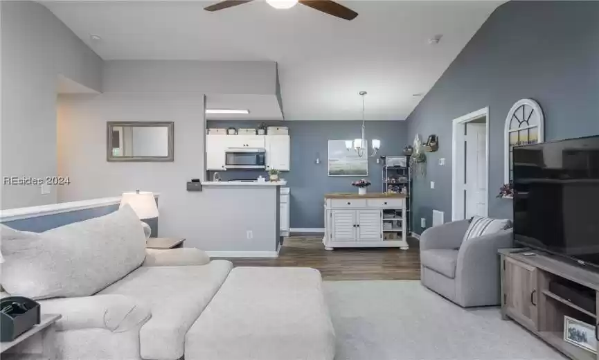 Living room featuring vaulted ceiling, wood-type flooring, and ceiling fan with notable chandelier