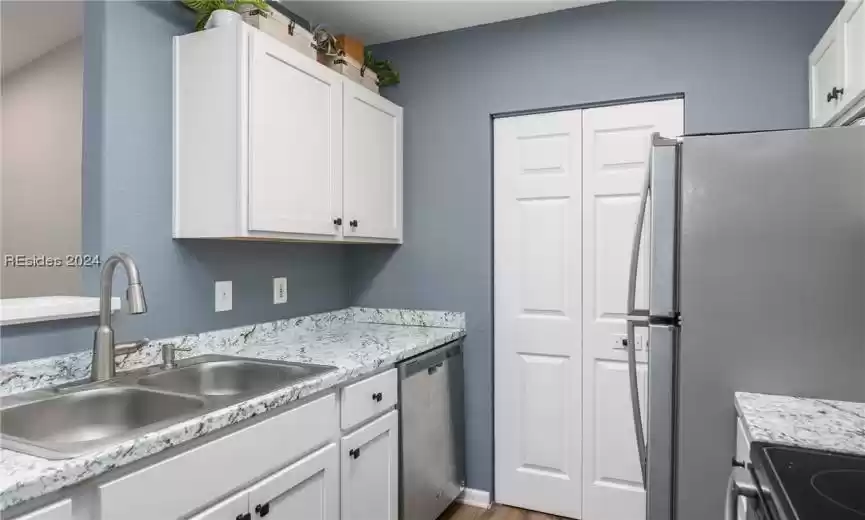 Kitchen with light stone counters, white cabinets, sink, hardwood / wood-style flooring, and appliances with stainless steel finishes