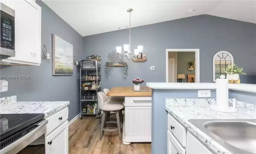 Kitchen featuring light wood-type flooring, hanging light fixtures, vaulted ceiling, stainless steel appliances, and a chandelier