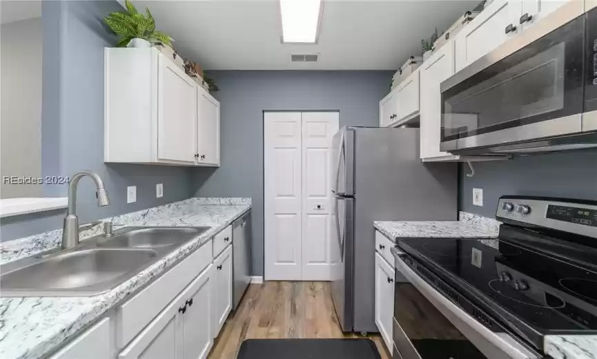 Kitchen featuring light wood-type flooring, white cabinets, light stone countertops, sink, and stainless steel appliances