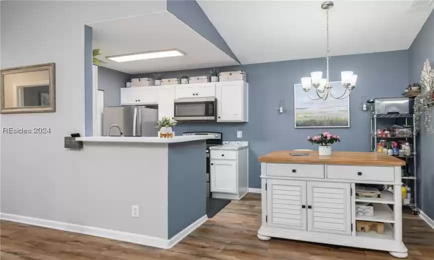 Kitchen with dark hardwood / wood-style flooring, an inviting chandelier, white cabinetry, hanging light fixtures, and appliances with stainless steel finishes