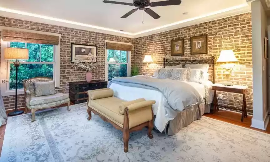 Bedroom with crown molding with under-mount lighting, heart pine floors,  brick wall feature and ceiling fan.