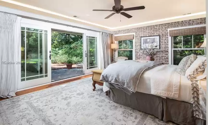Bedroom featuring decorative brick wall feature and slider access to private patio and lush, large yard.