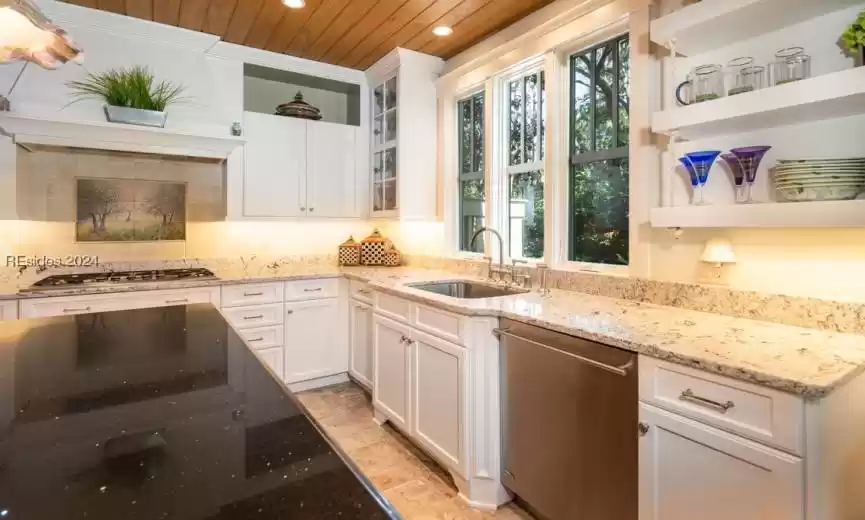 Kitchen with custom exhaust hood, stainless steel gas cooktop, light granite counters, and tasteful backsplash.