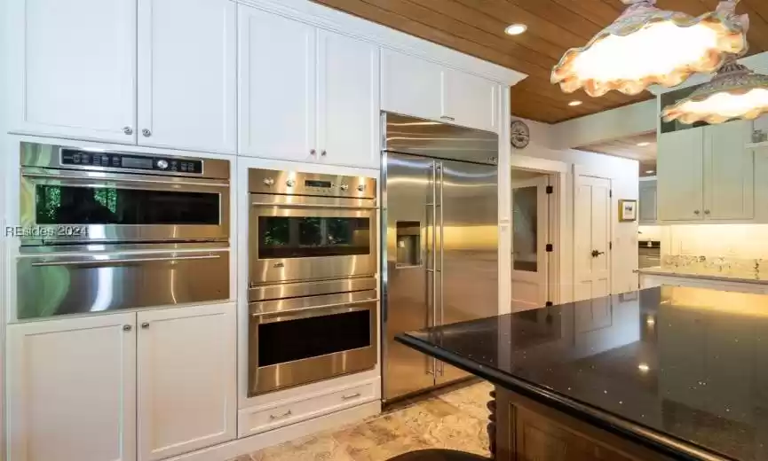 Kitchen featuring wood ceiling, light saturnia tile flooring, white cabinets, dark and light granite countertops, and GE Monogram stainless steel appliances.