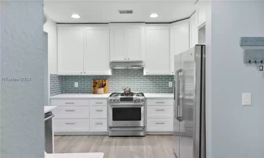 Kitchen featuring high end appliances, light hardwood / wood-style flooring, tasteful backsplash, and white cabinets